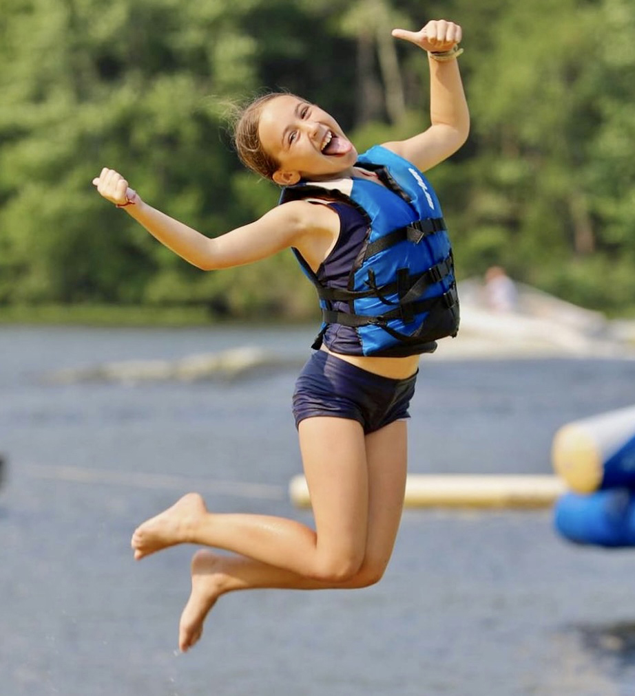 Girl camper jumping at the lake.