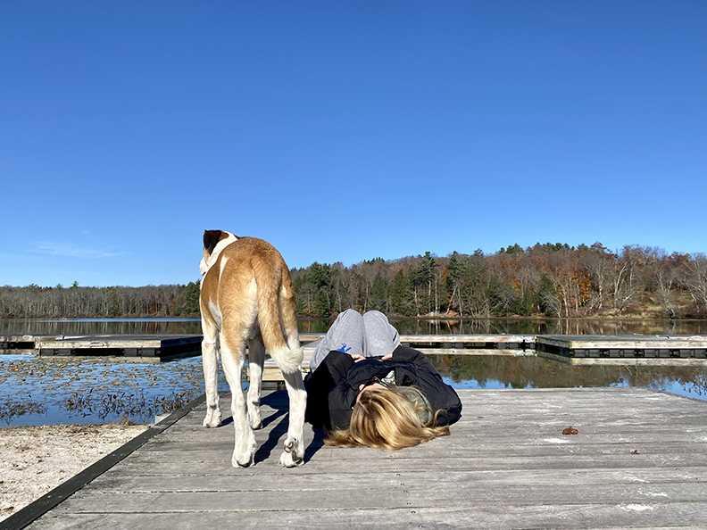 A camper and her dog enjoy a peaceful moment by the lake at Chestnut Lake Camp, capturing the beauty of nature and the special bond between them.