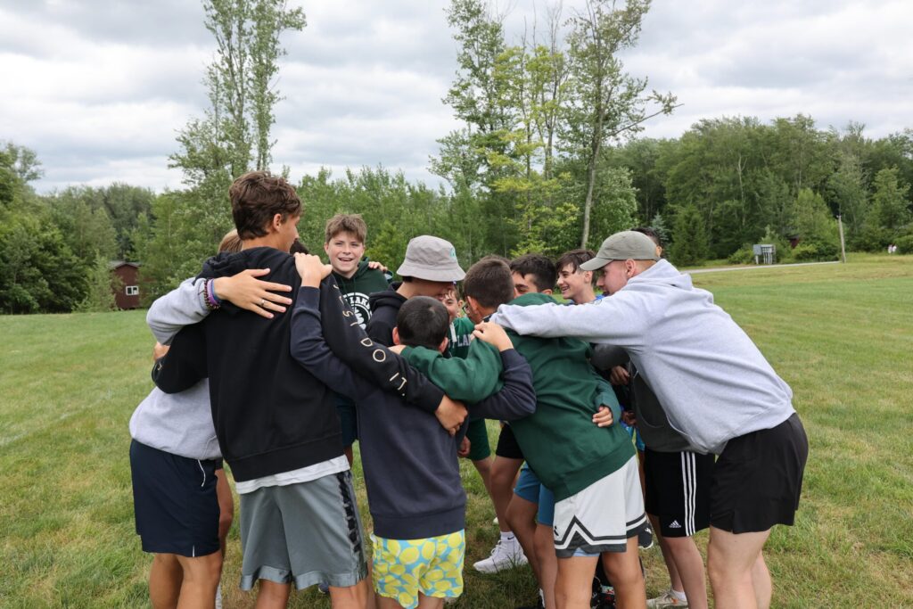 A group of campers huddle together during a football game at Chestnut Lake Camp, showcasing teamwork, strategy, and the thrill of friendly competition.