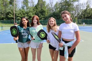 Four female campers play pickleball, enjoying a summer of fun, friendship, and outdoor adventure
