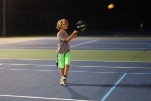 A young boy plays pickleball on the court, embracing the fun and excitement of summer sports